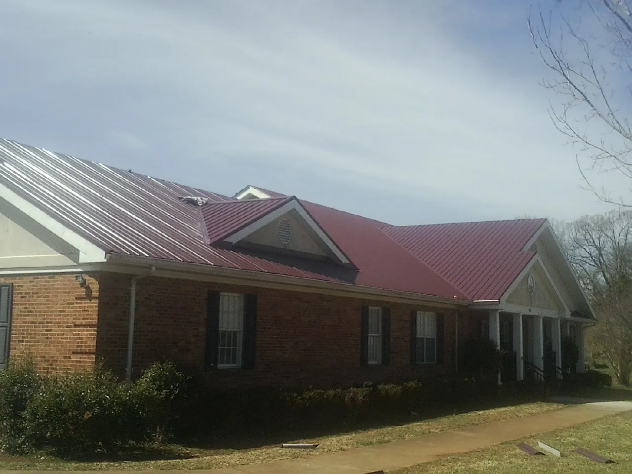 Red metal roof with gabled entries on a long brick building, from a Hail Damage Roof Repair job in Spencer