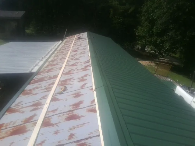 Old rusted panels beside newly installed green metal roofing — Wind Damage Roof Repair by Roofing Brothers in Spencer