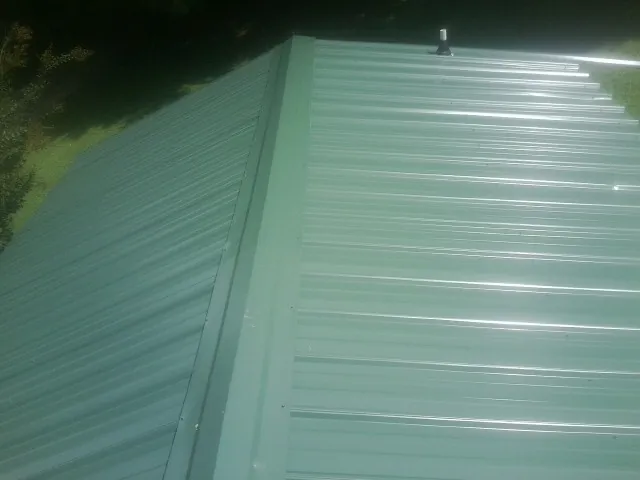 New green metal panels meeting at the ridge of a roof — Flat Roof Repair work by our crew in Spencer