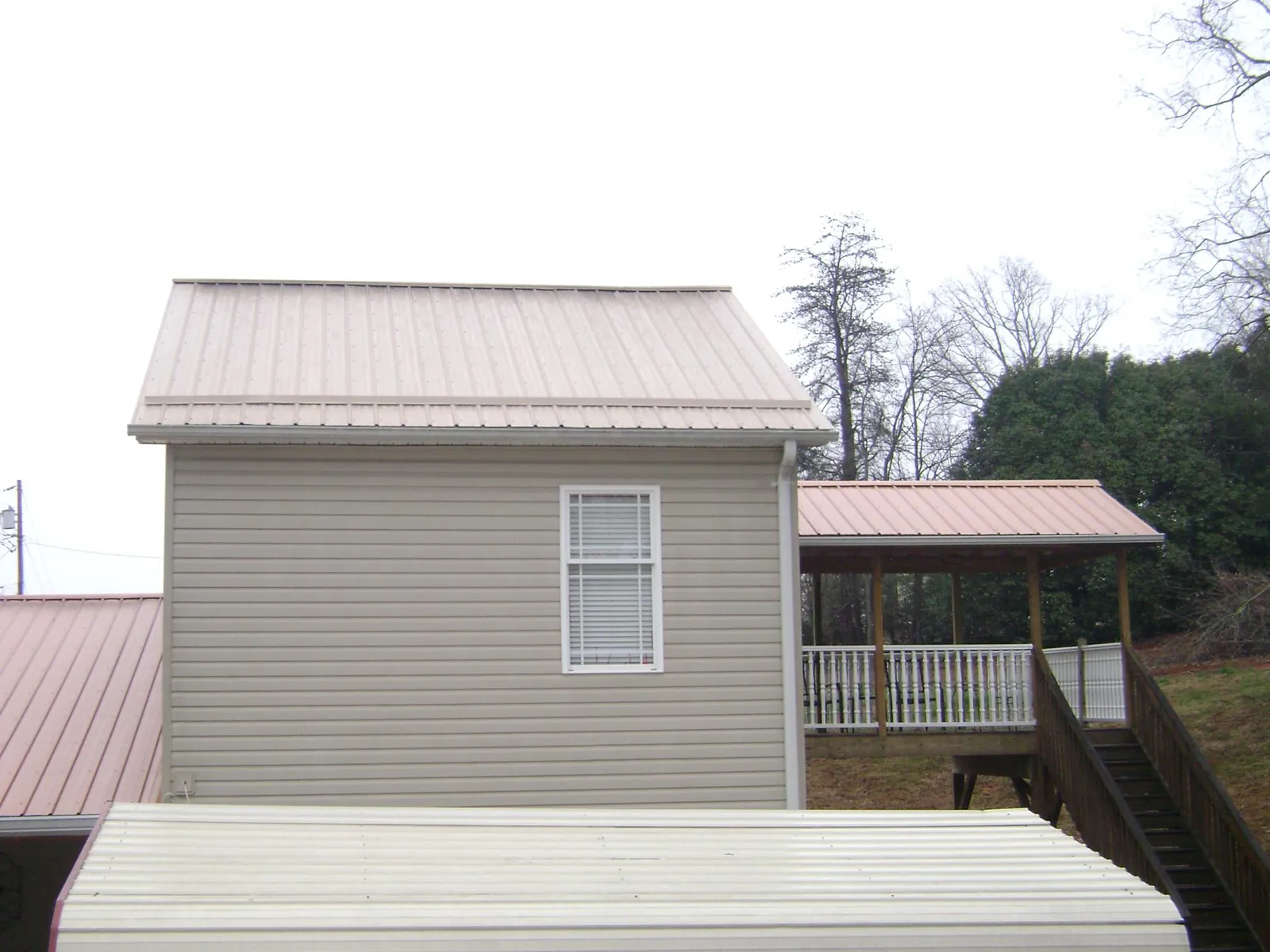 Tan metal roofs on a two story addition and attached porch, from a Roof Replacement job in Spencer